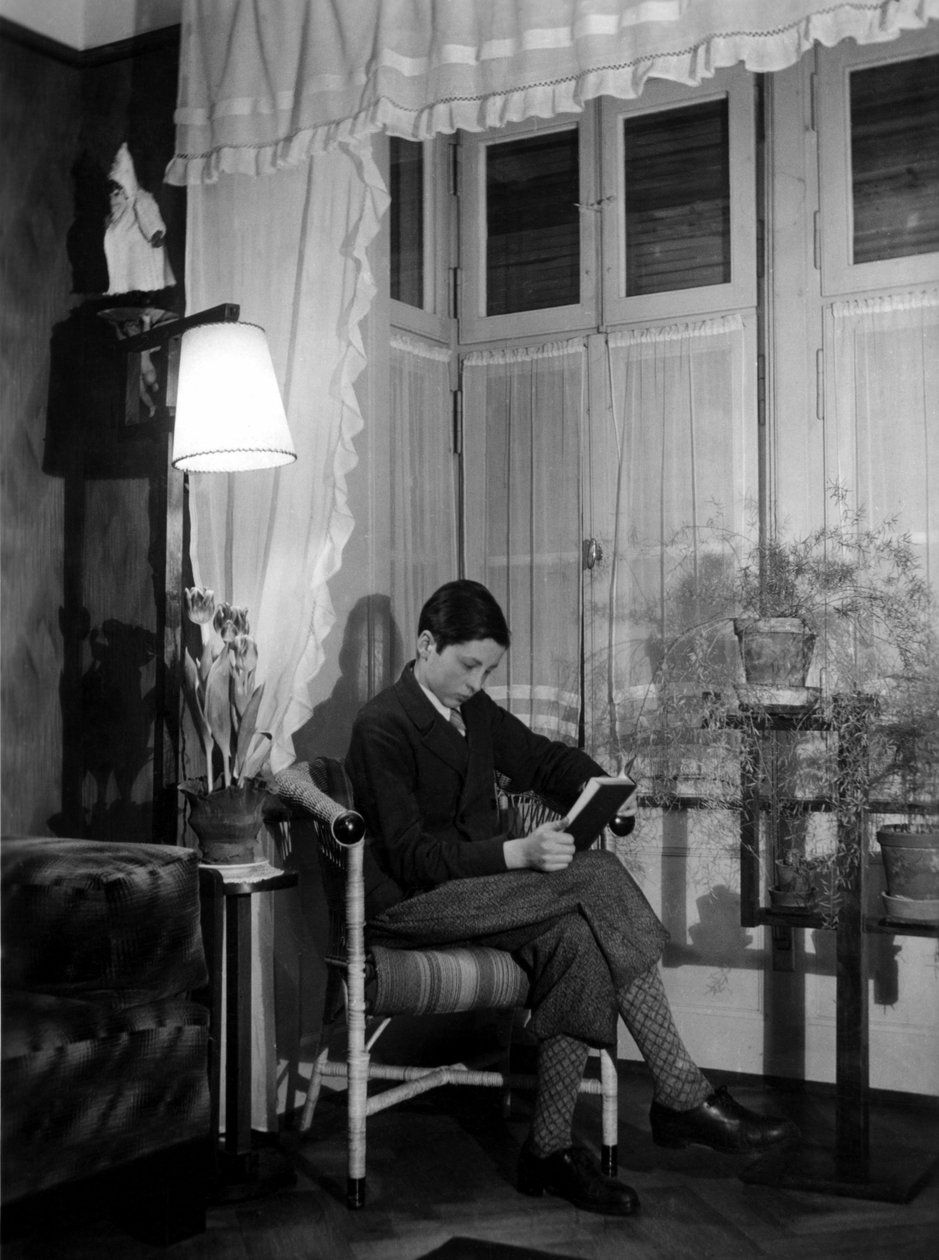 Porvarillisessa sisustuksessa istuva teini lukee kirjaa, hänellä on lyhyet housut ja korkeat sukat. 1915. Historiallinen valokuva, nainen lukemassa, n. 1915. tekijältä Unbekannter Künstler