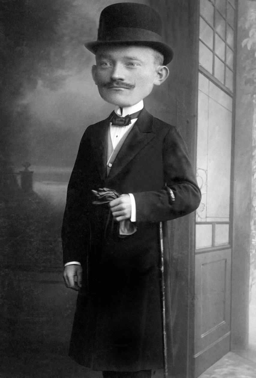 Muotokuva erittäin tyylikkäästä miehestä, jolla on jättiläisen pää, hänellä on melonihattu, keppi, rusetti ja musta takki. Tämä on valokuvamontaasi. Annees 1910 Historiallinen valokuva, jättiläispääinen mies tekijältä Unbekannter Künstler