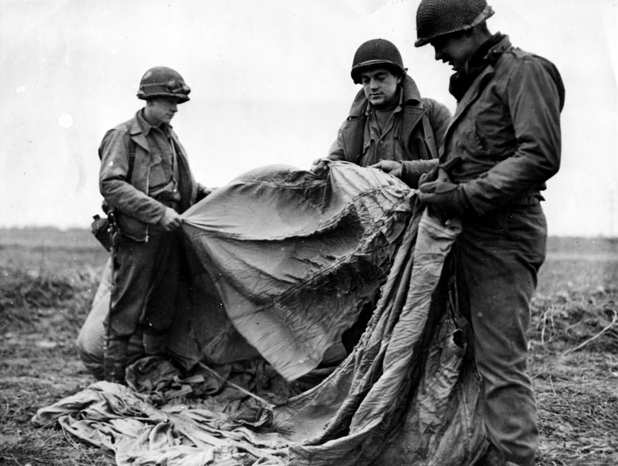 Toinen maailmansota (1939-1945) - Toinen maailmansota (WWII tai WW2): Kornelmunsterin lähellä (Saksa) 17. joulukuuta 1944: Yhdysvaltain 1. armeijan jalkaväki tutkii saksalaista laskuvarjoa, jota käytettiin iltana ennen operaatiokaartin hajoamista Reinillä  tekijältä Unbekannt