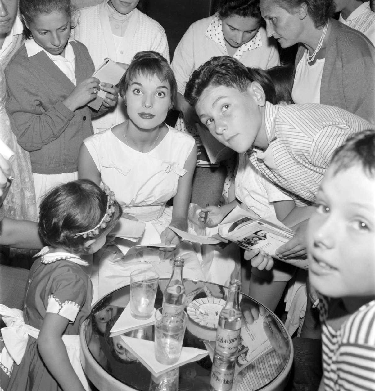 NÄYTTÄJÄ JA MUOTIMALLI ELSA MARTINELLI XVIII KANSAINVÄLISELLÄ ELOKUVIAALILLA VENETSIAN LIDOLLA (hän jakaa nimikirjoituksia nuorten fanien kanssa. Pöydällä pullo Schweppesiä) - 1957 tekijältä Unbekannt