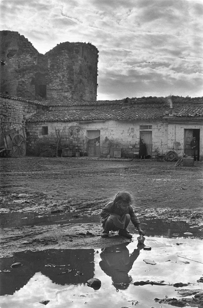 Nuori tyttö leikkii paperiveneellä lätäkkössä mudan ympäröimänä, Venosa, Basilicata, Italia tekijältä Unbekannt