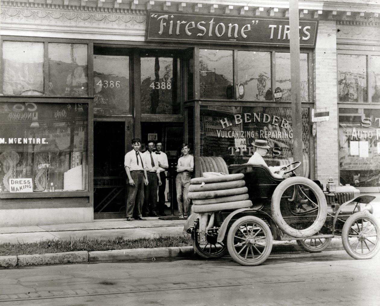 Miehet ja autonrenkaiden korjausauto kokoontuivat H.Bender Firestone Tire -jälleenmyyjän ulkopuolelle osoitteessa 4388 Olive Street tekijältä Unknown