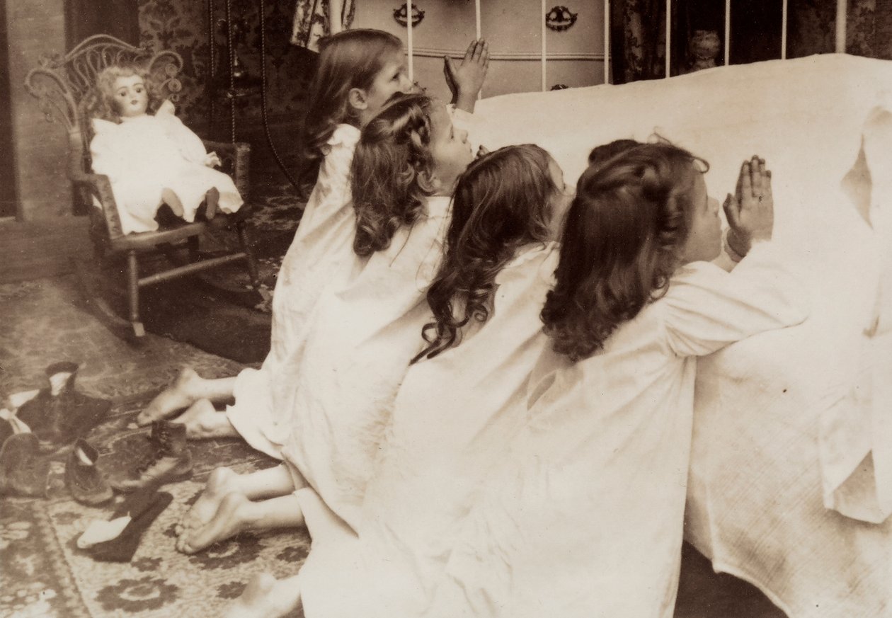 Neljä pientä tyttöä polvistuu sängyn vieressä iltarukousta lausuen. tekijältä Unknown photographer