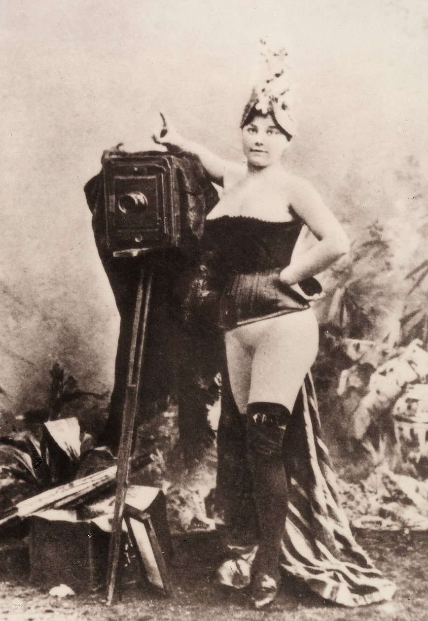 Muotokuva osittain alastomasta naisesta, joka nojaa antiikkiseen kameraan. tekijältä Unknown photographer
