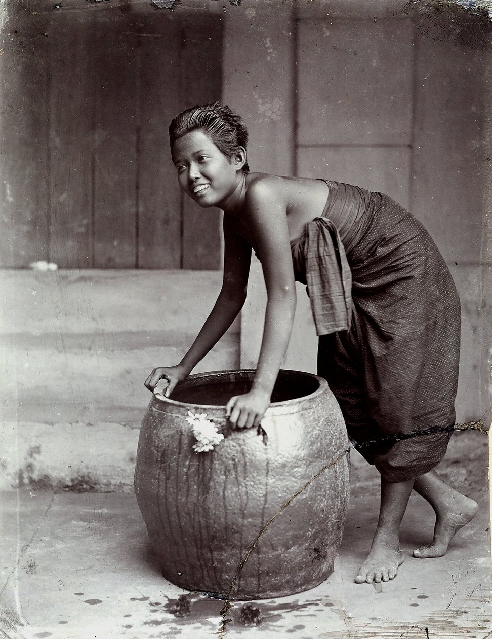 Nuori hymyilevä thaimaalainen nainen työntämässä suurta säiliötä. tekijältä Unknown photographer