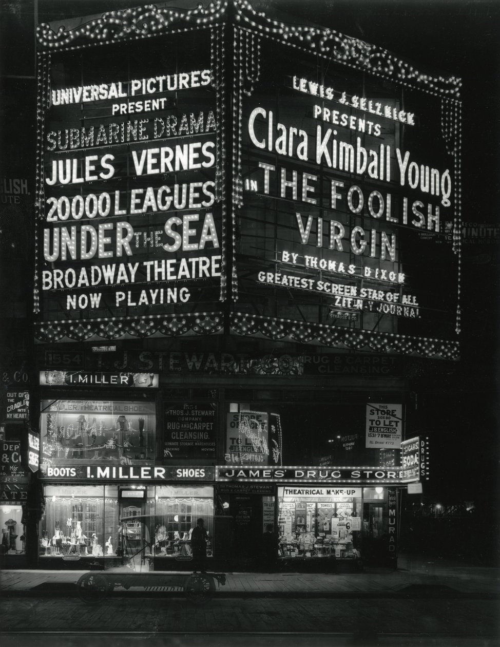 1554 Broadway osoitteessa 46th Street, I. Miller Shoes; James Drug Store ja suuret elokuvateltat valaistuivat yläpuolella. tekijältä William Davis Hassler