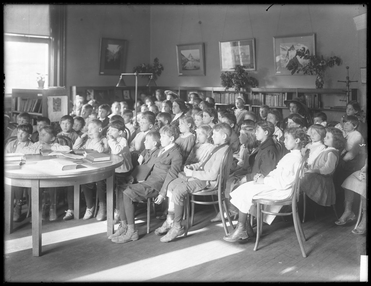 Lapset istuvat ja kuuntelevat Queens Borough Public Libraryn tunnistamattoman haaran lukusalissa, n. 1910 tekijältä William Davis Hassler