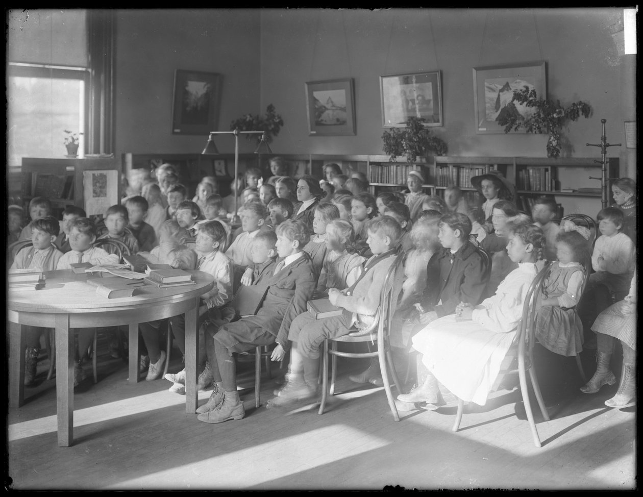 Lapsia istumassa ja kuuntelemassa Queens Borough Public Libraryn tunnistamattoman haarakonttorin lukusalissa, noin 1910. tekijältä William Davis Hassler