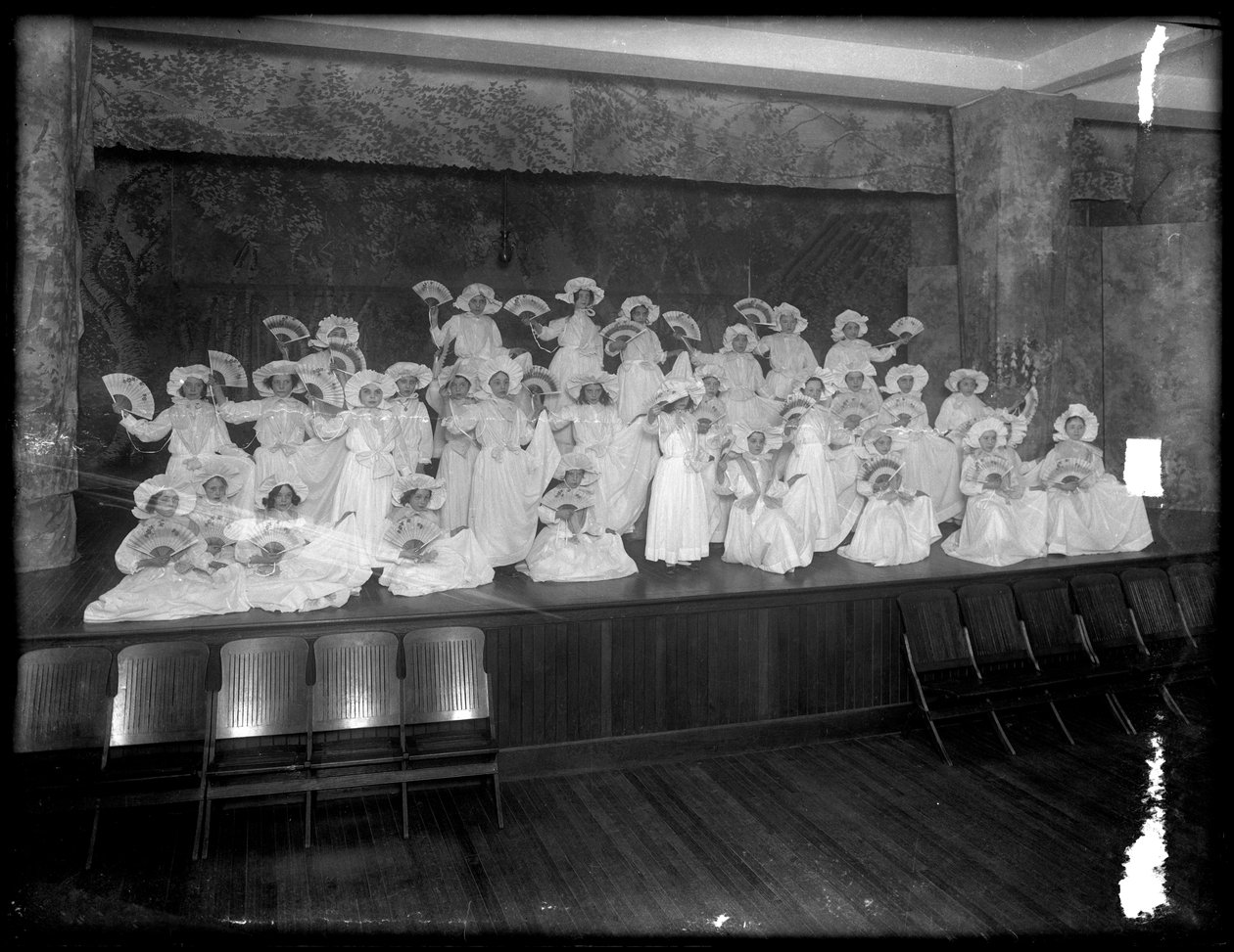 Ryhmä pieniä tyttöjä poseerasi pienellä lavalla faneja pitäen, luultavasti roomalaiskatolinen orpojen turvapaikka, Kingsbridge, Bronx, n. 1911 tekijältä William Davis Hassler