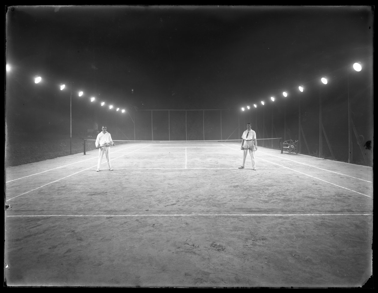 Kaksi nuorta miestä tuntemattomalla savisella tenniskentällä yöllä, heinäkuu 1915. tekijältä William Davis Hassler