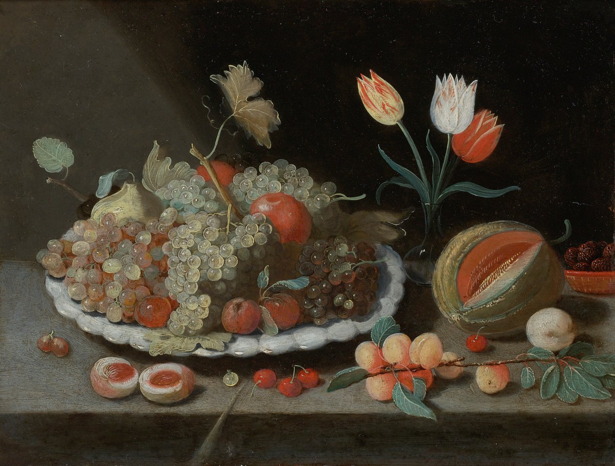 Asetelma viinirypäleillä ja muilla hedelmillä lautasella, lasimaljakko tulppaaneilla, meloni, aprikoosit, kirsikat ja muut hedelmät, kaikki reunalla tekijältä Workshop of Jan van Kessel the Elder