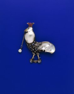 Käsityökillan valkoinen ja keltainen metallirintaneula "kruunatun" kukon muodossa, jossa on kuplahelmiä, helmiä, safiireja, turmaliinia ja kuukiviä, n. 1905 (metalli, helmet, safiirit, turmaliinit, kuukivet) tekijältä Charles Robert Ashbee