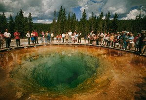Puiston kävijät kokoontuvat sinivihreän, kukanmuotoisen lämpöaltaan ympärille. Yellowstone Nati...