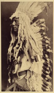 Vanha henkilö, Piegan. Nuoret miehet eivät kaipaa julkisia juhlia pukeutuakseen soturi-isänsä vaatteisiin. Kuva otettu Edward S. Curtisin (1868-1952) Pohjois-Amerikan intiaaneja käsittelevän tietosanakirjan osasta 6, jossa on etuosa tekijältä Edward Sheriff Curtis