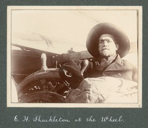 E H Shackleton seisoo Discovery-aluksen ratissa (1901) Sir Ernest Henry Shackletonin albumista National Antarctic Expedition (1901-1903). tekijältä Ernest Henry Shackleton