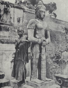Nuori buddhalainen noviisi munkki Buddha-patsaan vieressä, Ranskan Indokiinassa (m/v kuva)