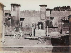 Osittainen näkymä Pompejissa sijaitsevan Marcus Lucretiuksen talon korotettuun puutarhaan, joka on koristeltu marmoripatsailla ja hermeillä. Keskellä suihkulähde kapealla. Taustalla katkelmia seinämaalauksista tekijältä Giorgio Sommer