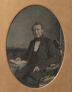 Istuva mies osoittaa kohtaa avoimessa kirjassa, 1850-luku.