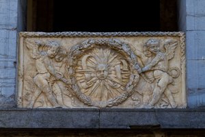 Kaidelevy, jossa säteilevä aurinko seppeleessä, bareljeef San Sebastianon kirkon julkisivussa