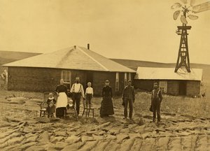 Kotitalousperhe, heidän turvetalonsa ulkopuolella, jossa on tuulimylly viereisen rakennuksen katolla Custerin piirikunnassa, Nebraskassa, n. 1885 (b/w kuva) tekijältä Solomon D. Butcher