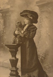 [Sarah Bernhardt seisoo ateljeeympäristössä ja pitää pientä mustaa koiraa koristeellisella, veistetyllä puujalustalla] tekijältä Theodore C. Marceau