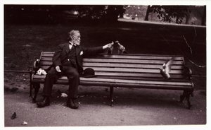 Mies puistonpenkillä, n. 1920 Tuntemattoman valokuvaajan ottama valokuva puistonpenkillä istuvasta miehestä ruokkimassa kyyhkysiä noin vuonna 1920 tekijältä Unbekannt