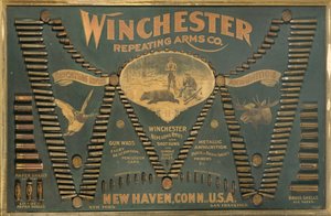 Winchester Cartridge -näyttötaulu, jossa on kattava valikoima metalli-, messinki- ja paperikoteloisia kivääri- ja haulikapurukkeja, jotka on järjestetty laajennetun "W"-kirjaimen muotoon. tekijältä Unbekannt