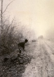Aamusumuun kietoutunut maantie. Etualalla mies halkoo kiviä - tekijältä Unbekannter Künstler