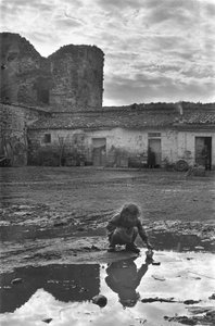 Nuori tyttö leikkii paperiveneellä lätäkkössä mudan ympäröimänä, Venosa, Basilicata, Italia tekijältä Unbekannt