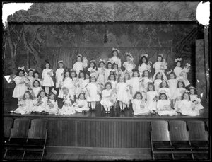Ryhmä pieniä tyttöjä poseerasi pienellä näyttämöllä pitäen nukkeja, luultavasti roomalaiskatolinen orpojen turvapaikka, Kingsbridge, Bronx, n. 1911