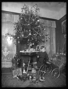 Seymour-poika poseerasi kolmipyörän kanssa joulukuusen vieressä salissa, jouluna 1912