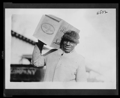 Afroamerikkalainen mies kantaa olkapäällään laatikkoa Four Roses -viskiä, jonka Yhdysvaltain verovirasto mahdollisesti takavarikoi tekijältä American Photographer