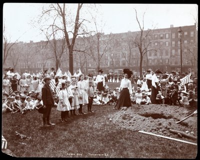 Aikuiset ja lapset pitelevät lippuja seisomassa juuri kaivetun reiän ympärillä puunistutusta varten Arbor Dayna Tompkins Square Parkissa, New Yorkissa, 1904 (hopeagelatiiniprintti) tekijältä Byron Company