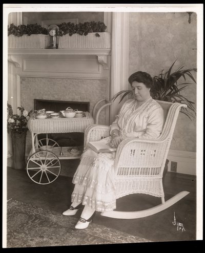Rouva Howard istuu kirjan kanssa keinutuolissa kotonaan osoitteessa 200, 5th Avenue, New York, 1915-1916 (hopeagelatiiniprintti) tekijältä Byron Company