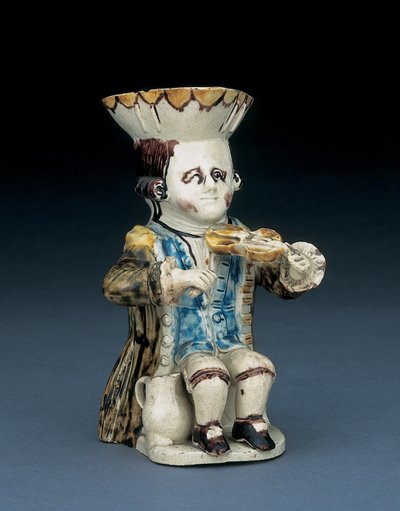 Viulunsoittajan toby-kannu, hattu ruskealla ja keltaisella särmäisellä reunalla, ruskeat hiukset viillottuna ja sidottu jonossa valkoisella ruusukkeella, pesty ruskea takki, n. 1770 tekijältä English School