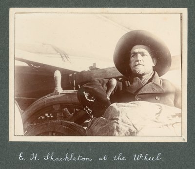 E H Shackleton seisoo Discovery-aluksen ratissa (1901) Sir Ernest Henry Shackletonin albumista National Antarctic Expedition (1901-1903). tekijältä Ernest Henry Shackleton