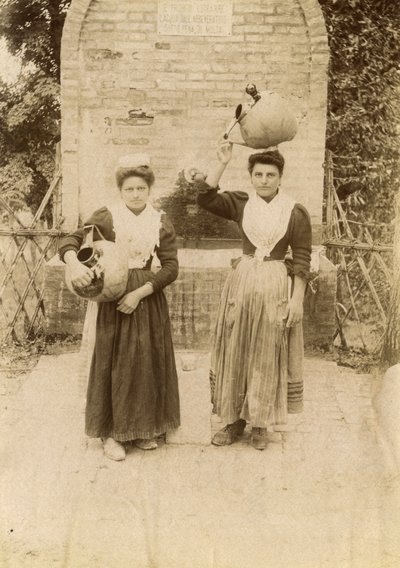Kaksi nuorta naista perinteisiin vaatteisiin pukeutuneena ja terrakottapurkkia kantaen kaivon lähellä, Marche, Italia, n. 1910. tekijältä Italian Photographer