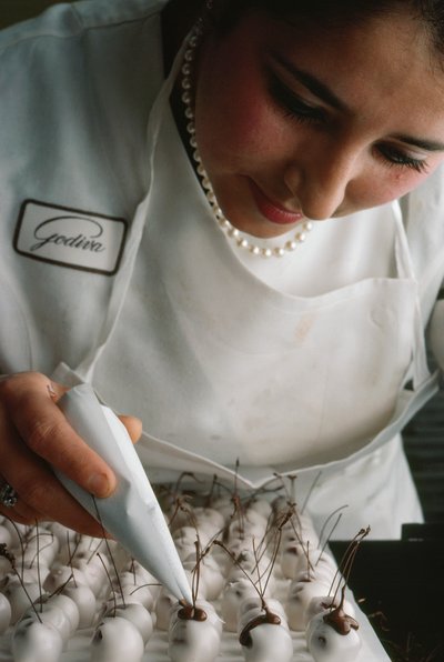 Godiva-kokki kiinnittää suklaanvarret fondantilla päällystettyihin kirsikoihin. Bryssel, Belgia. tekijältä James L Stanfield