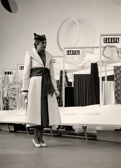 Malli "Lamma" -nimisen couture-talon luomassa päällystakissa. Artikkeli on koottu vyötäröllä leveällä ripsillä, ja se on täydennetty pehmeällä hatulla. Kuva on otettu kankaiden näyttelyyn tarkoitetussa salissa. (s/w-kuva) tekijältä Luis Bogino