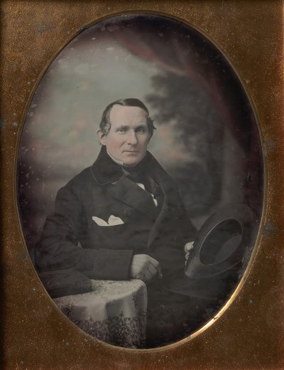 Mies, jolla on takki ja hanskat, pitelee hattua, istuu maalatun ulkotaustan edessä, 1840-luku. tekijältä Samuel Broadbent Jr..