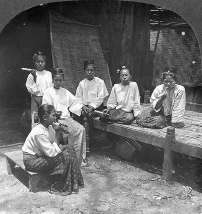 Burmalaiset naiset tupakoivat kodin ulkopuolella, Mandalay, Burma, 1908. tekijältä Stereo Travel Co