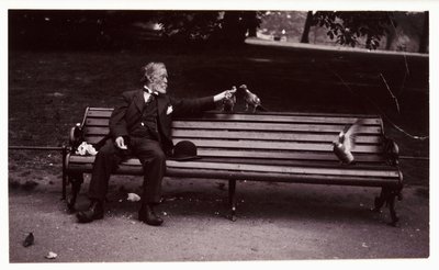 Mies puistonpenkillä, n. 1920 Tuntemattoman valokuvaajan ottama valokuva puistonpenkillä istuvasta miehestä ruokkimassa kyyhkysiä noin vuonna 1920 tekijältä Unbekannt
