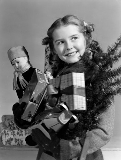 Nuori tyttö kantamassa käsivarsia joululahjoja, n. 1950 tekijältä Unbekannt