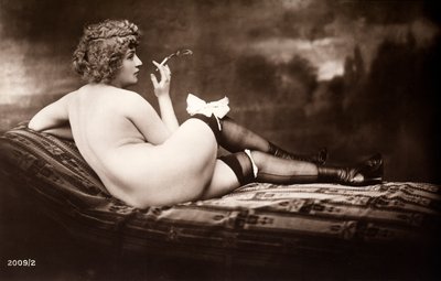 Muotokuva nuoresta naisesta, joka poseeraa alasti, selkä kääntyneenä, savuketta polttaessaan. tekijältä Unknown photographer