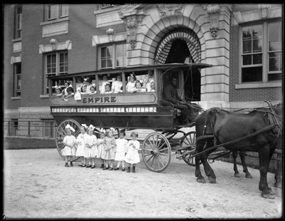 Pienet tytöt poseeraavat hevosvaunussa ja sen edessä, tuntemattoman rakennuksen edessä, luultavasti roomalaiskatolinen orpojen turvapaikka, Kingsbridge, Bronx, n. 1910 tekijältä William Davis Hassler