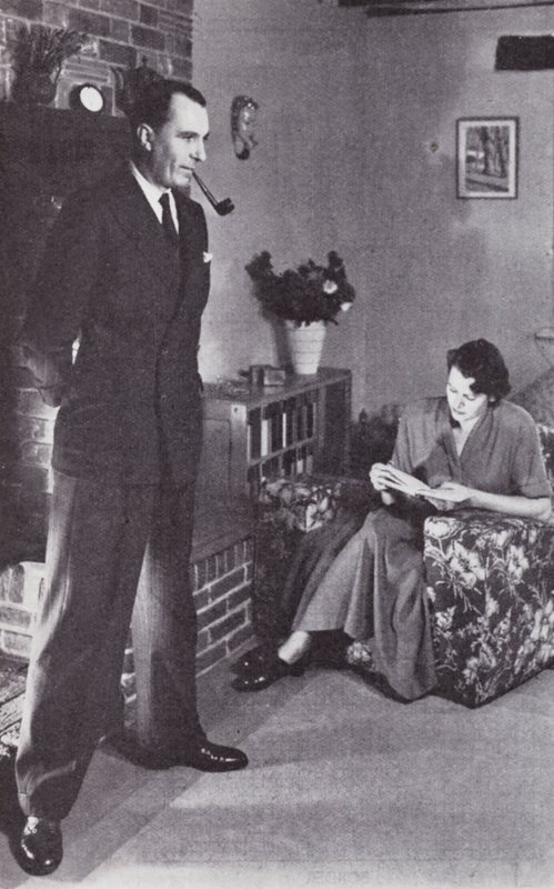 Vaimo lukee ja mies lämmittää selkänsä tulta vasten, n. 1950 tekijältä English Photographer