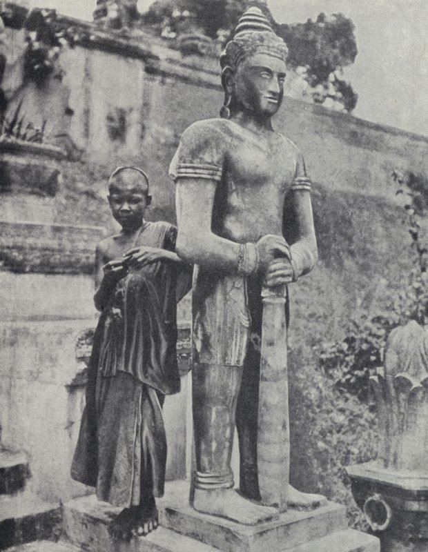 Nuori buddhalainen noviisi munkki Buddha-patsaan vieressä, Ranskan Indokiinassa (m/v kuva) tekijältä Ewing Galloway