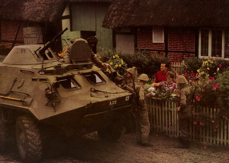 Kansallisen kansanarmeijan sotilaat toivottavat asukkaat sydämellisesti tervetulleeksi marssin tauon aikana (värikuva) tekijältä Photographer German