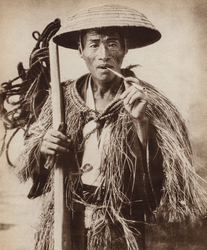 Japanilainen kuli (maatyöläinen) hattu päällään suojatakseen häntä rankalta sateelta riisipelloilla (m/w kuva) tekijältä Photographer Japanese