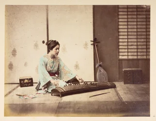 Laulavat tytöt [Japani], Studiomuotokuva nuoresta japanilaisesta naisesta, joka istuu tatamimatolla soittaen kielisoitinta,  Valokuvaaja: Tuntematon  Lucas Collection: Valokuvaennätys Charles Jamesin ja Morton P, Lucasin maailmankiertueesta